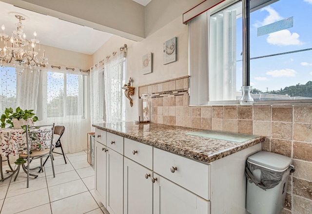 kitchen featuring backsplash, dark stone counters, white cabinets, a notable chandelier, and light tile floors