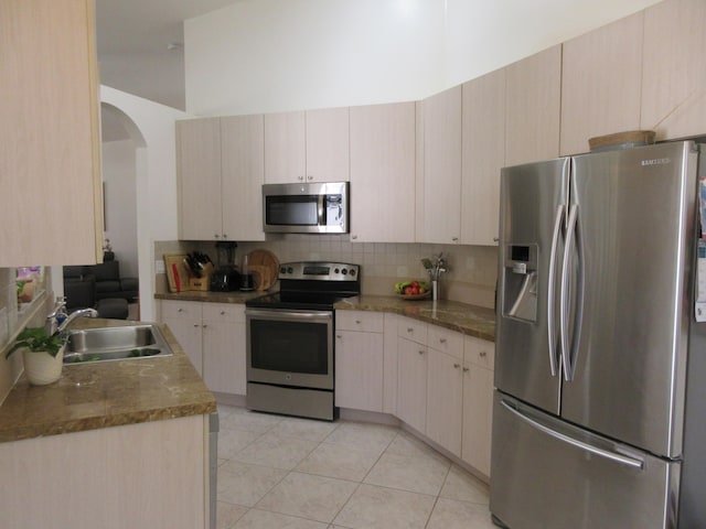 kitchen with light tile patterned flooring, backsplash, light stone counters, stainless steel appliances, and sink