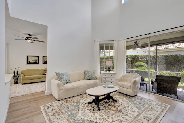 living room with ceiling fan, light wood-type flooring, and a high ceiling