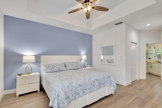 bedroom with a tray ceiling, light hardwood / wood-style flooring, ceiling fan, and ensuite bathroom