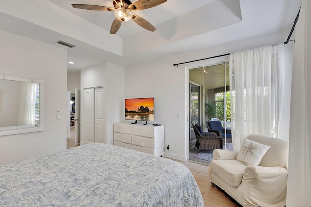 bedroom with a closet, ceiling fan, light hardwood / wood-style floors, a raised ceiling, and access to outside