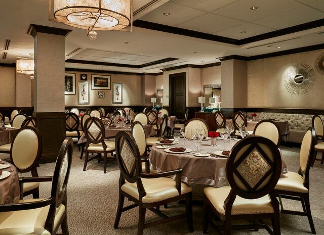 carpeted dining area with a raised ceiling, a paneled ceiling, crown molding, and ornate columns