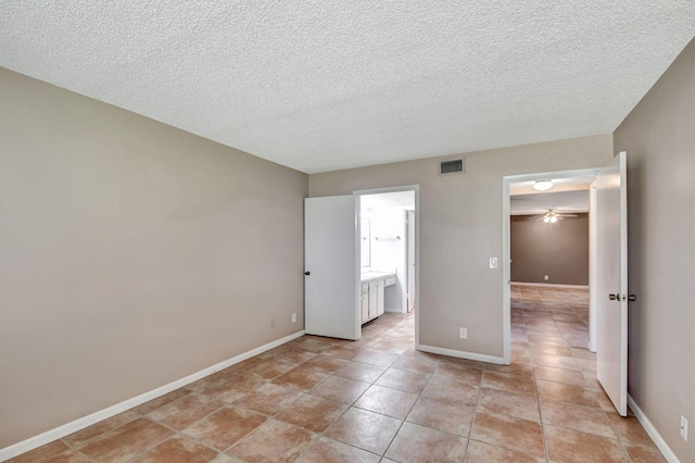 unfurnished bedroom with connected bathroom, a walk in closet, light tile floors, and a textured ceiling