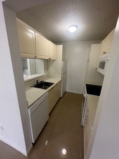 kitchen featuring white appliances, a textured ceiling, white cabinetry, sink, and tile floors