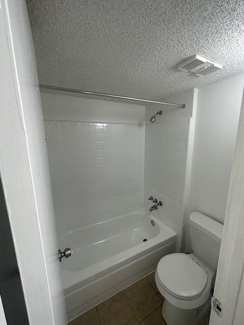 bathroom with tiled shower / bath, toilet, tile floors, and a textured ceiling