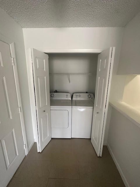 laundry area featuring a textured ceiling, washing machine and dryer, and dark tile floors