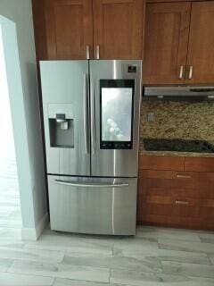 kitchen featuring stainless steel fridge with ice dispenser, stone counters, fume extractor, and black cooktop