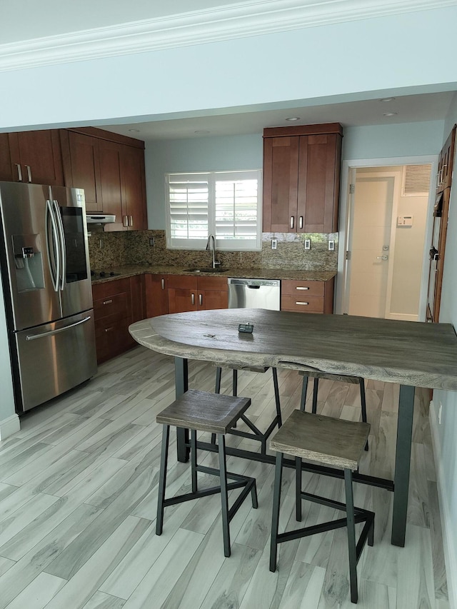 kitchen with sink, backsplash, crown molding, stainless steel appliances, and dark stone countertops