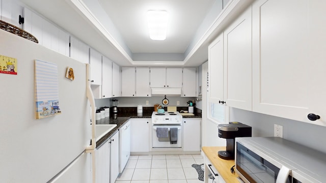 kitchen featuring dark stone counters, a raised ceiling, white cabinetry, white appliances, and light tile floors