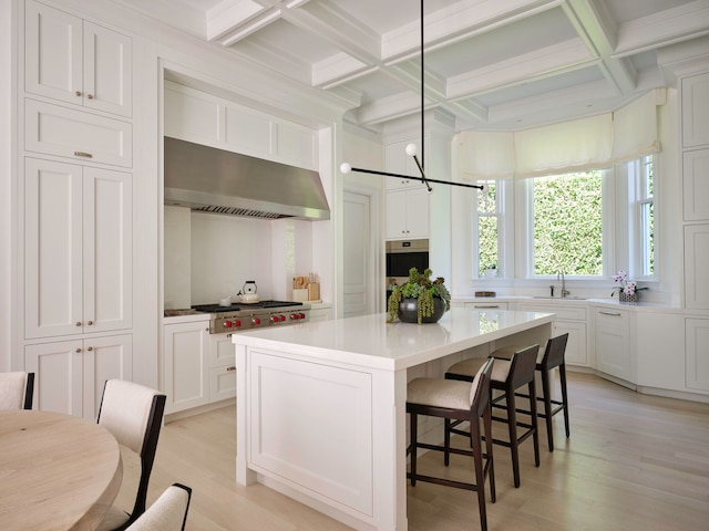 kitchen with decorative light fixtures, coffered ceiling, light hardwood / wood-style flooring, a kitchen island, and stainless steel appliances