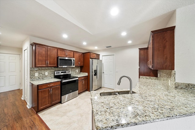 kitchen with light stone counters, stainless steel appliances, tasteful backsplash, sink, and light tile floors