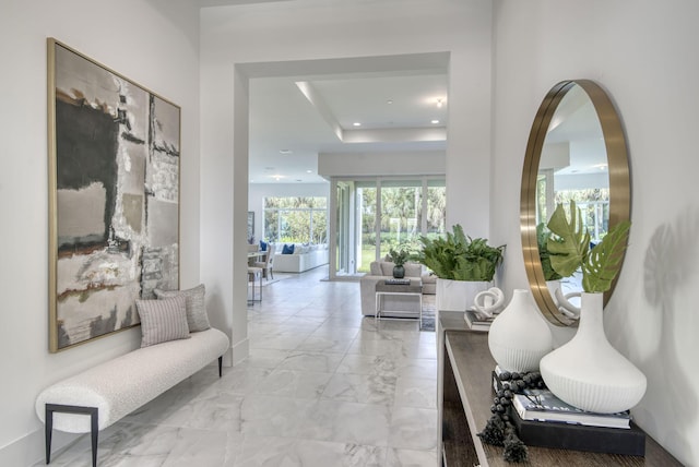 hall featuring marble finish floor, a tray ceiling, and recessed lighting