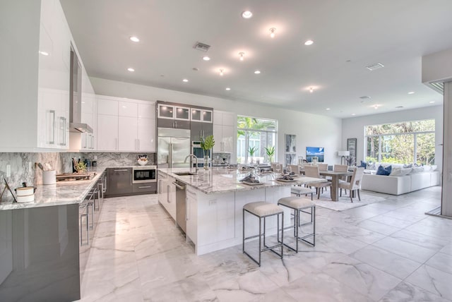 kitchen with a breakfast bar area, white cabinets, built in appliances, sink, and a spacious island