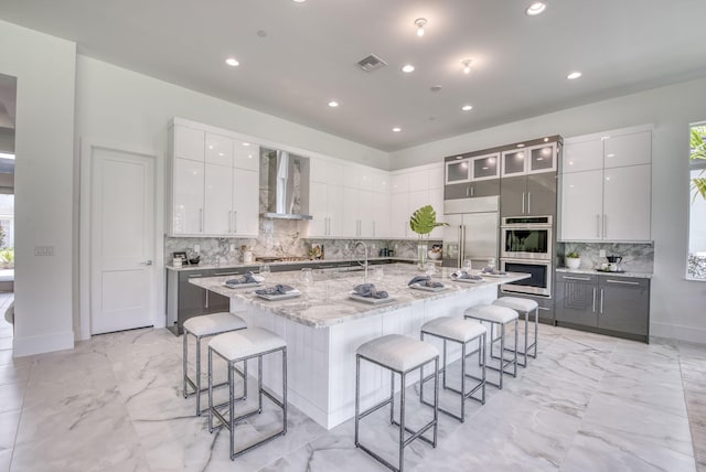 kitchen with appliances with stainless steel finishes, wall chimney exhaust hood, modern cabinets, a kitchen bar, and a center island with sink