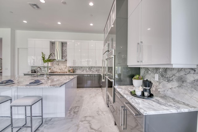 kitchen featuring a sink, visible vents, white cabinets, wall chimney exhaust hood, and modern cabinets