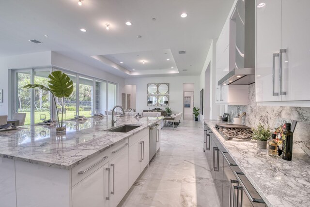 kitchen with a raised ceiling, wall chimney range hood, light stone countertops, light tile patterned floors, and sink