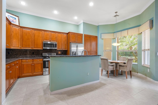 kitchen featuring appliances with stainless steel finishes, pendant lighting, an island with sink, decorative backsplash, and dark stone counters