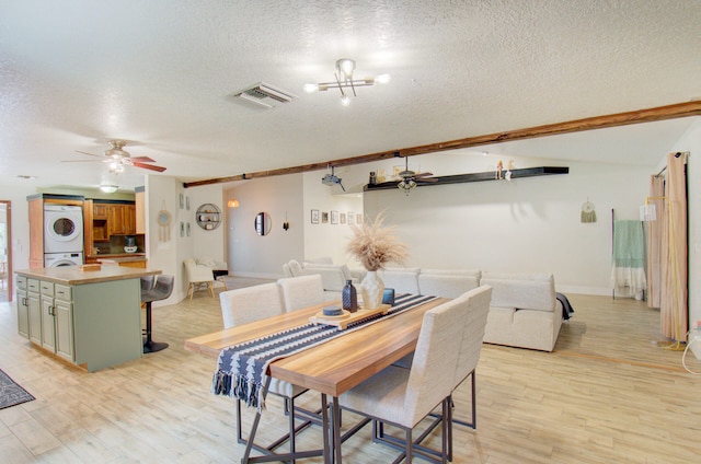 dining space featuring a textured ceiling, ceiling fan with notable chandelier, light hardwood / wood-style floors, and stacked washer and clothes dryer