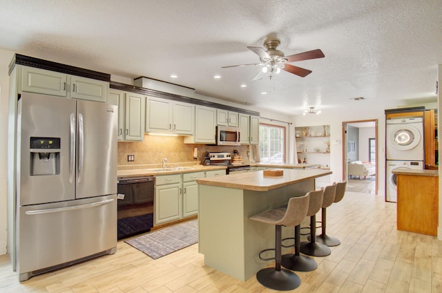 kitchen featuring a kitchen bar, stainless steel appliances, sink, stacked washer and dryer, and a kitchen island