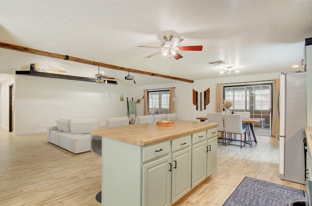 kitchen featuring a kitchen island, a textured ceiling, ceiling fan, light wood-type flooring, and stainless steel fridge