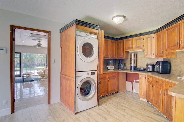 laundry area with ceiling fan, stacked washer and dryer, light hardwood / wood-style floors, and a textured ceiling