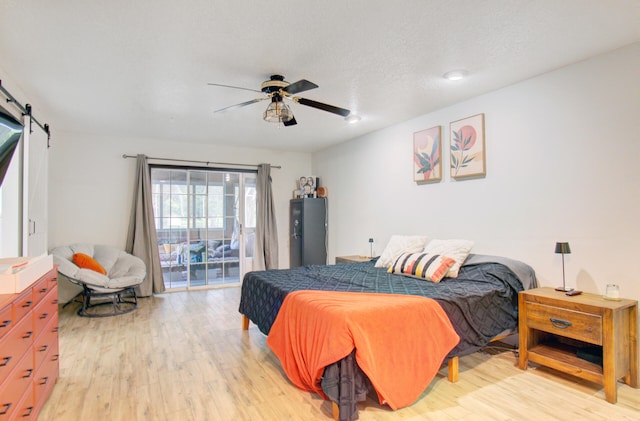 bedroom with access to exterior, light wood-type flooring, a textured ceiling, ceiling fan, and a barn door