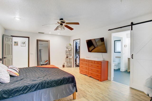 bedroom featuring ensuite bath, ceiling fan, a barn door, hardwood / wood-style flooring, and a spacious closet