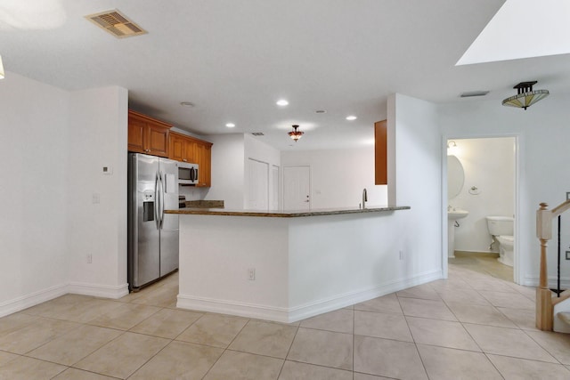 kitchen with light tile patterned floors, stainless steel appliances, kitchen peninsula, and dark stone counters