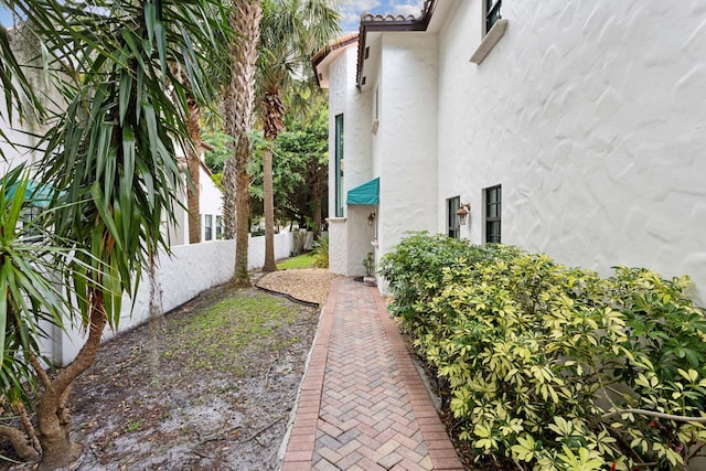 view of side of home featuring a tile roof, fence, and stucco siding