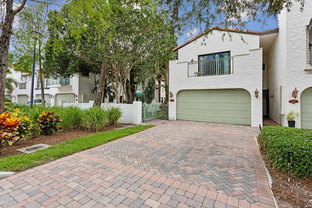 view of front facade featuring a balcony, fence, an attached garage, stucco siding, and decorative driveway