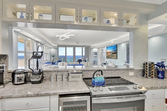 kitchen featuring wine cooler, stainless steel range with electric stovetop, white cabinetry, and plenty of natural light