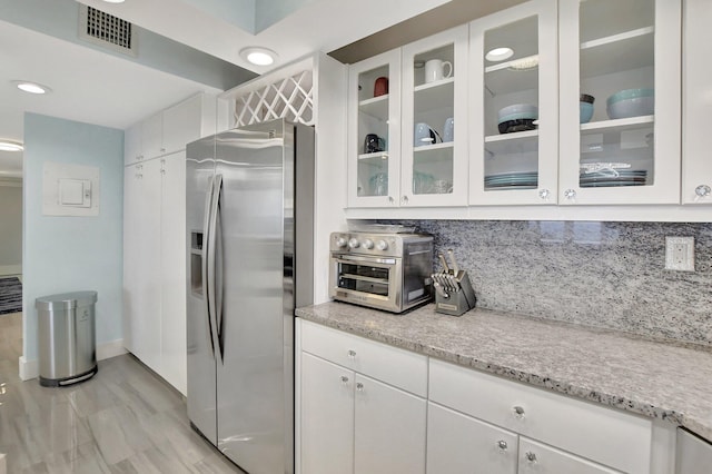 kitchen featuring backsplash, light stone counters, stainless steel fridge with ice dispenser, and white cabinetry