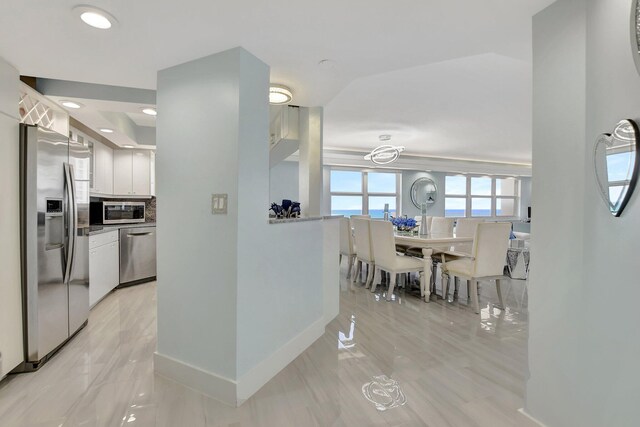 kitchen with appliances with stainless steel finishes, backsplash, light tile flooring, and white cabinets