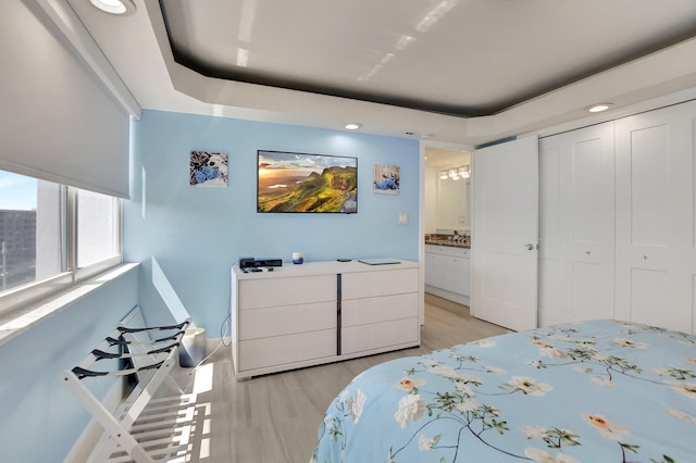 bedroom with a tray ceiling, light hardwood / wood-style floors, and a closet