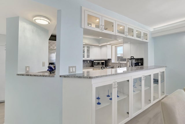 kitchen with light stone counters, white cabinets, backsplash, stainless steel microwave, and kitchen peninsula