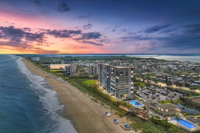 aerial view at dusk featuring a water view and a beach view