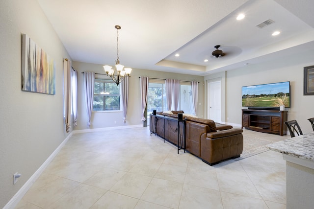 living room with a tray ceiling, light tile floors, and ceiling fan with notable chandelier