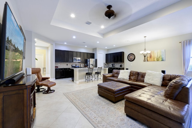 living room with a tray ceiling, light tile flooring, and an inviting chandelier