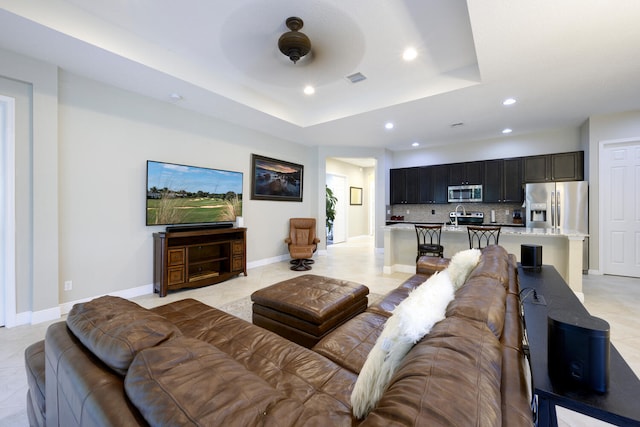 living room with ceiling fan, a tray ceiling, and light tile floors