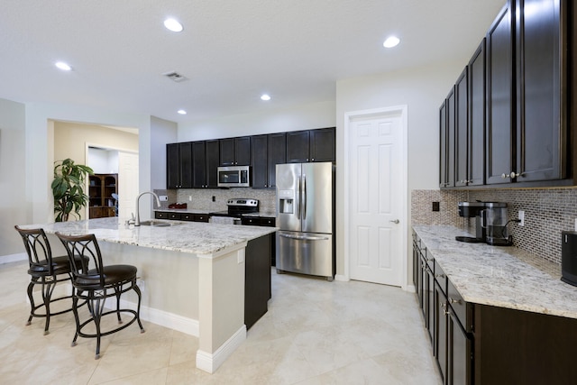 kitchen with light stone countertops, tasteful backsplash, sink, a kitchen island with sink, and appliances with stainless steel finishes