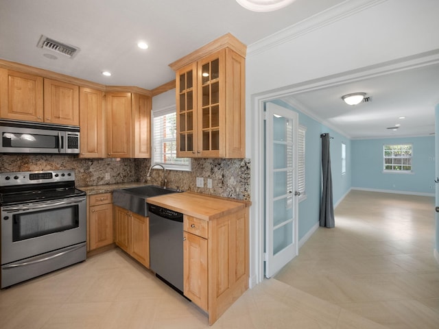 kitchen featuring crown molding, stainless steel appliances, light tile floors, sink, and tasteful backsplash