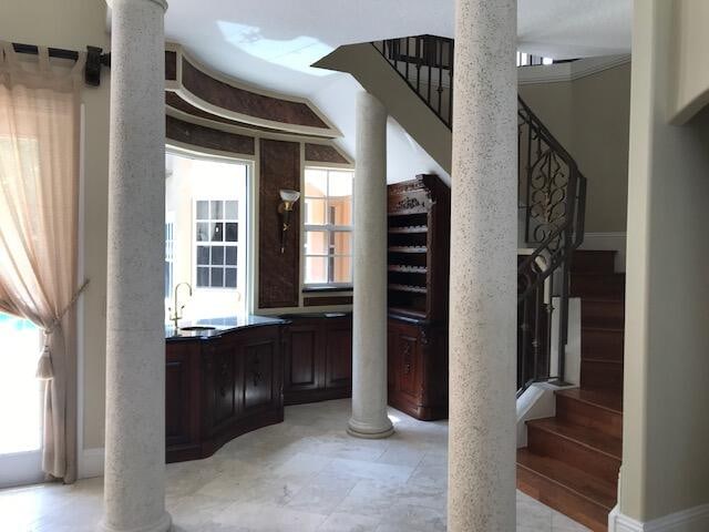 bar featuring a healthy amount of sunlight, dark brown cabinets, light tile floors, and decorative columns