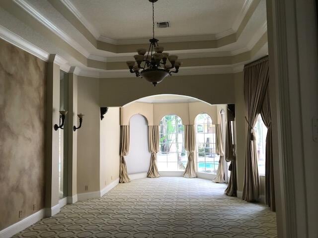 interior space with a chandelier, carpet floors, a raised ceiling, and ornamental molding