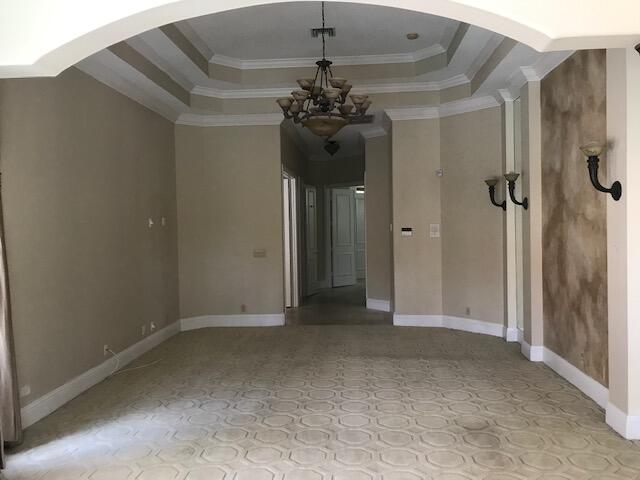 tiled empty room featuring a chandelier, a raised ceiling, and crown molding