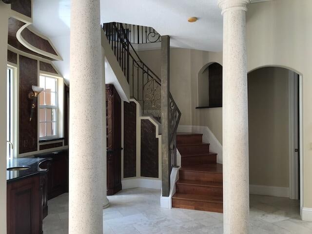 stairs with light tile flooring, decorative columns, and sink