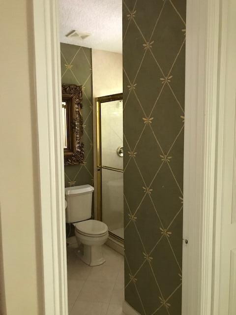 bathroom featuring a textured ceiling, tiled shower, toilet, and tile flooring