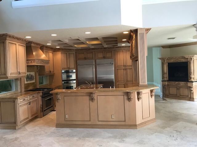 kitchen featuring a kitchen island with sink, crown molding, custom range hood, stainless steel appliances, and coffered ceiling