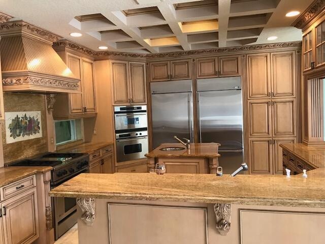 kitchen featuring light stone countertops, premium range hood, premium appliances, coffered ceiling, and sink