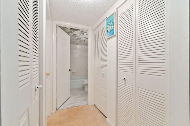 hall with a textured ceiling and light tile patterned flooring