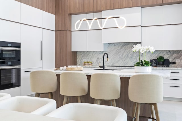 kitchen with a breakfast bar, sink, tasteful backsplash, white cabinetry, and stainless steel double oven